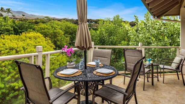 Een ronde tafel met vier stoelen, een parasol en een vaas met bloemen op een balkon met uitzicht op groen en bergen.