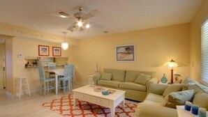 A living room with a sofa, a coffee table, a dining area with chairs, and a ceiling fan.