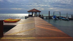 Un muelle de madera que lleva a un pabellón junto al mar, con barcos amarrados cerca.