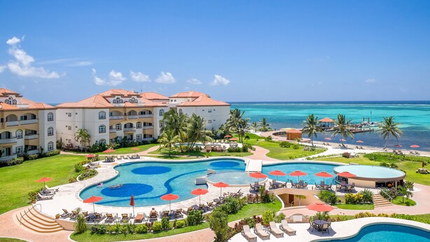 Un resort con varias piscinas, una playa y un edificio grande con balcones.