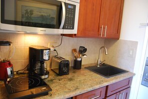 Une cuisine équipée d’un four à micro-ondes, d’un grille-pain, d’un mixeur, d’une machine à café, d’un évier et de meubles de rangement en bois.