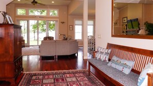 A spacious living room with a large window, a wooden coffee table, and a sofa with patterned cushions. - Modern St Michaels estate -Pier, Pool, Gas fire pit, Bikes, Kayaks (Easton)