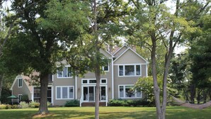 A two-story house with a front porch, surrounded by trees and a hammock. - Modern St Michaels estate -Pier, Pool, Gas fire pit, Bikes, Kayaks (Easton)