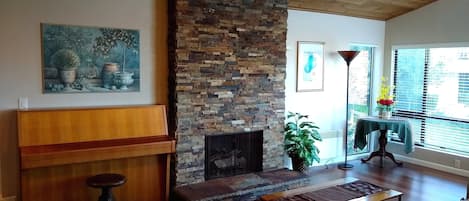 Un salón con chimenea de piedra, muebles de madera, un cuadro y una ventana con vistas.