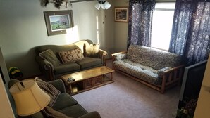 Una sala de estar con un sofá, un sillón más pequeño, una mesa de centro y una lámpara.