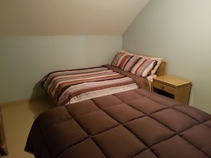 A bedroom with two beds, a nightstand, and a sloped ceiling.