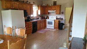 Una cocina con armarios de madera, un refrigerador blanco, una estufa y un lavavajillas. Hay una mesa de comedor con sillas y una alfombra en el suelo.