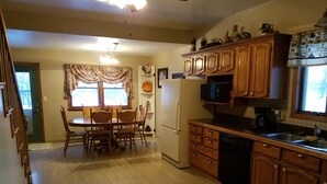 Una cocina con armarios de madera, un refrigerador, un microondas y una zona de comedor con una mesa y sillas.