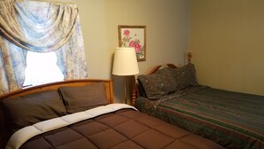 Un dormitorio con cama, mesita de noche, lámpara y ventana con cortinas.