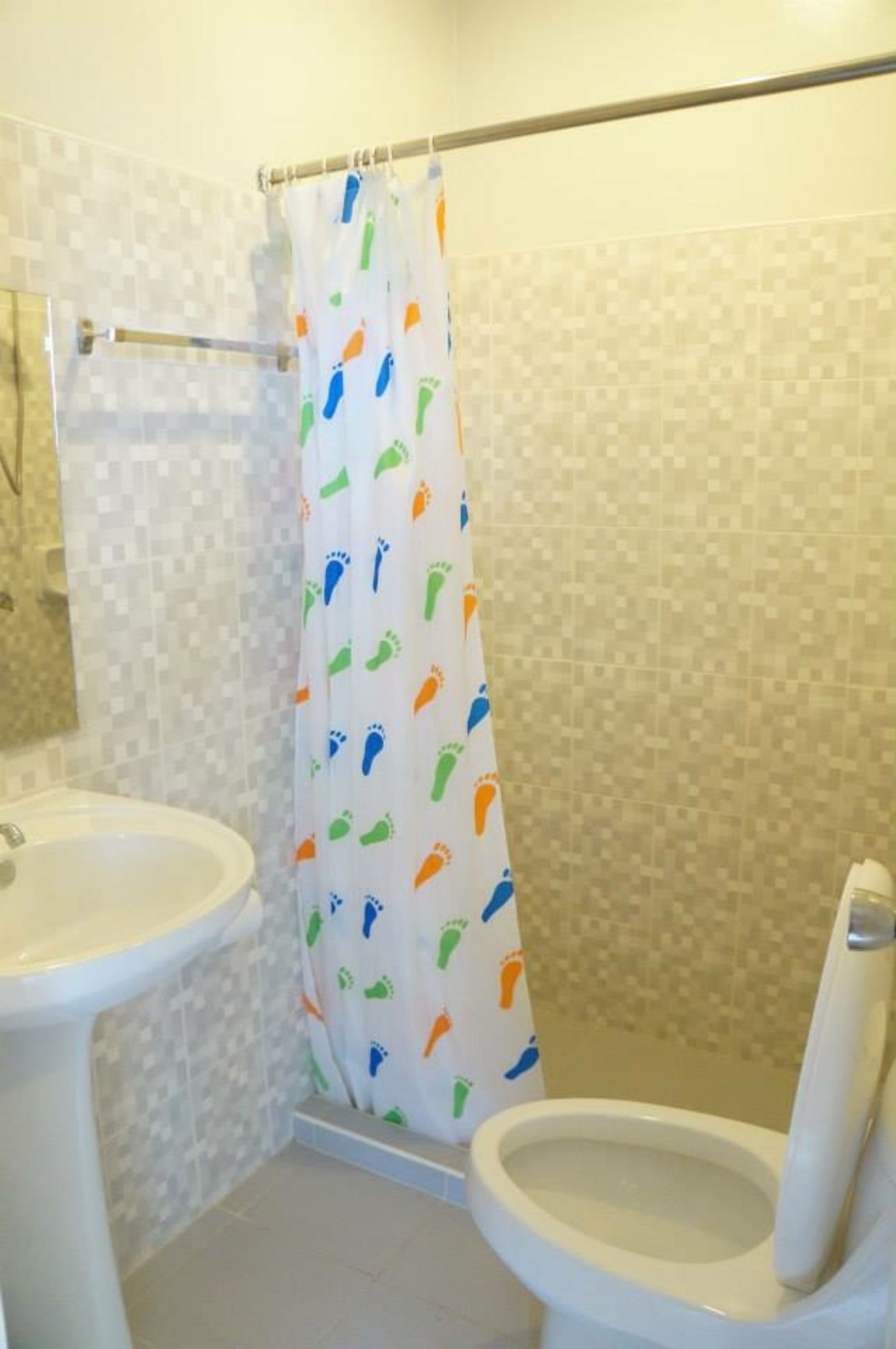 A bathroom with a toilet, sink, and shower curtain with a playful pattern.