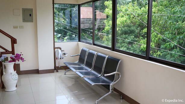 Un área de espera con un banco, un jarrón blanco con flores, y una ventana que ofrece vistas al verdor.