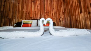 A hotel room with a wooden wall, a bed with white bedding, and two towels arranged in a heart shape. - Palmsuay Resort (Khao Saming)