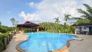 A swimming pool with a curved edge, surrounded by a tiled deck and a covered pavilion. - Palmsuay Resort (Khao Saming)