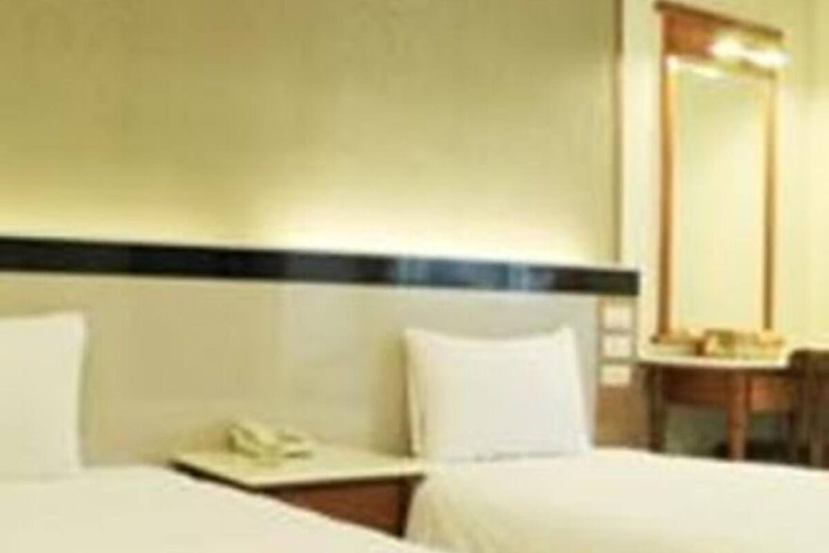 A hotel room with two beds, a bedside table with a lamp, and a mirror on the wall.