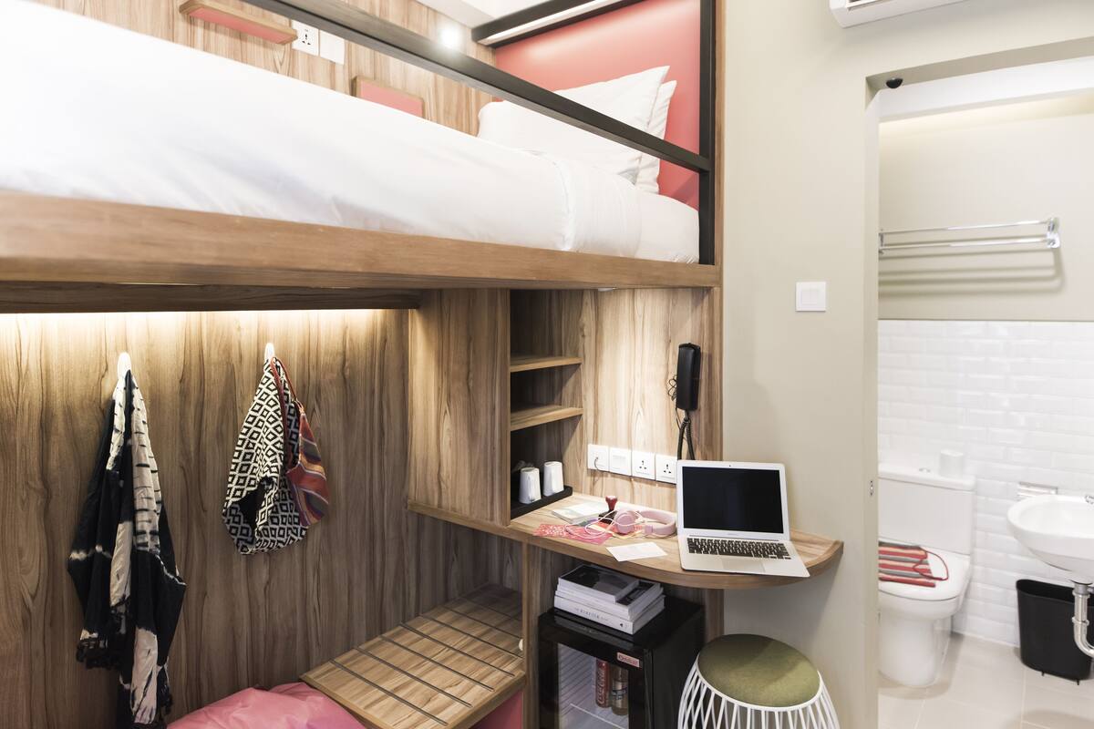 A bunk bed with a laptop on a shelf, a toilet, and a sink in a modern bathroom.