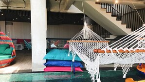 A pool area with a hammock, colorful cushions, and a floating chair. - Cara Cara Inn (Kuta)