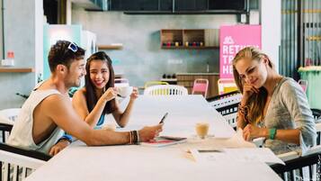 Tres personas sentadas en una mesa en un café moderno, con un menú a la vista y un letrero que dice 'RETURN TO HEAT'.