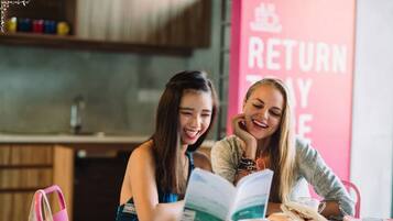 Two people sitting at a table with a book and a cup, in a room with a 'RETURN TO YOUR' sign.