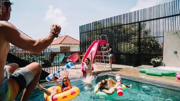 A swimming pool with inflatable rings, a slide, and a fenced area with chairs and a ladder.