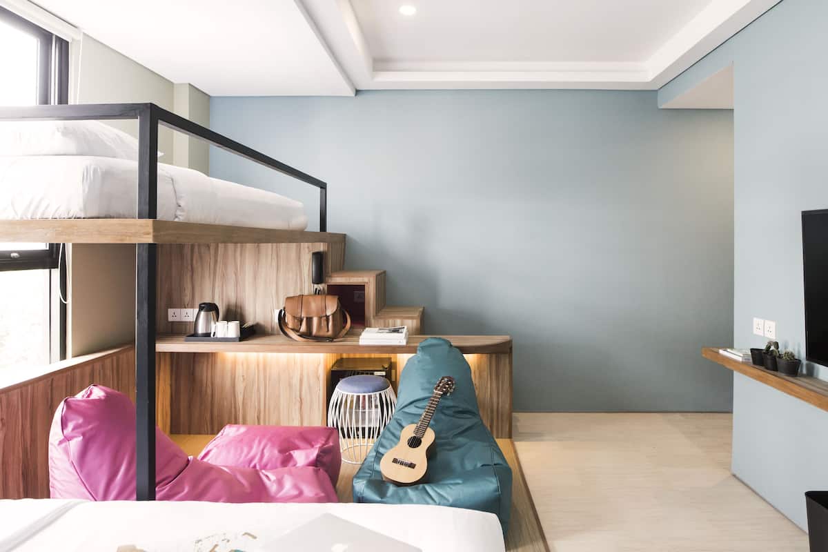 A modern room with a bunk bed, a desk with a laptop, a guitar, and a window with a view.
