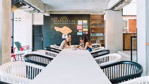 A modern interior with a central table surrounded by white and black chairs, a ceiling fan, and a wall with a map and various signs. - Cara Cara Inn (Kuta)
