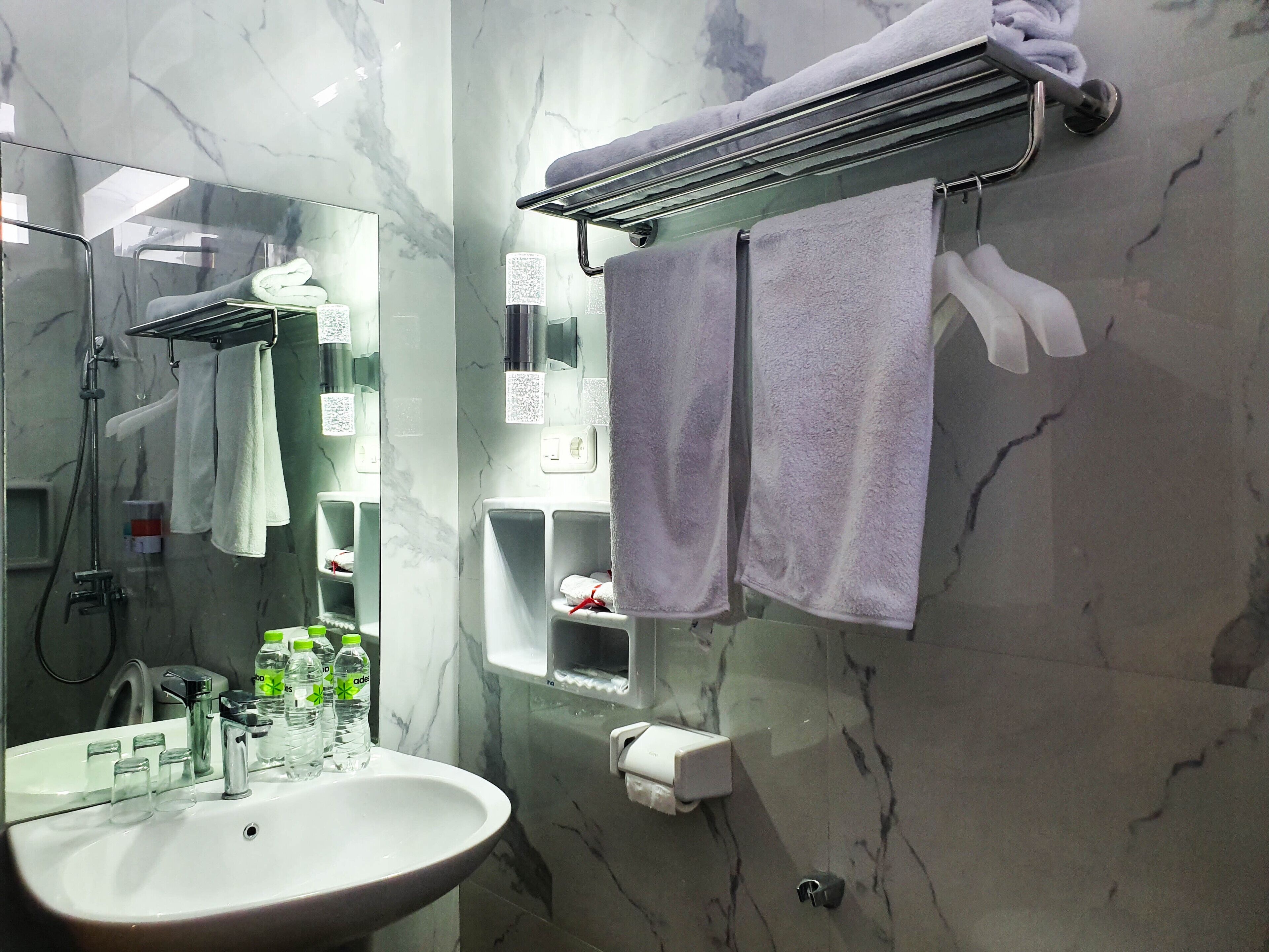 Ein Badezimmer mit Marmorwand, einem Waschbecken mit Glasbehältern, einem Handtuchhalter mit Handtüchern und einem Spiegel.