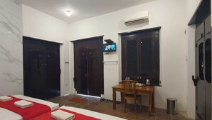 A hotel room with two beds, a small dining table, a TV, and an air conditioning unit.