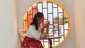 A person sitting at a table by a window with a view of the street.