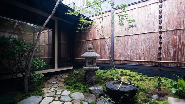 A traditional Japanese garden with a stone pathway, moss, a stone lantern, and a bamboo fence.