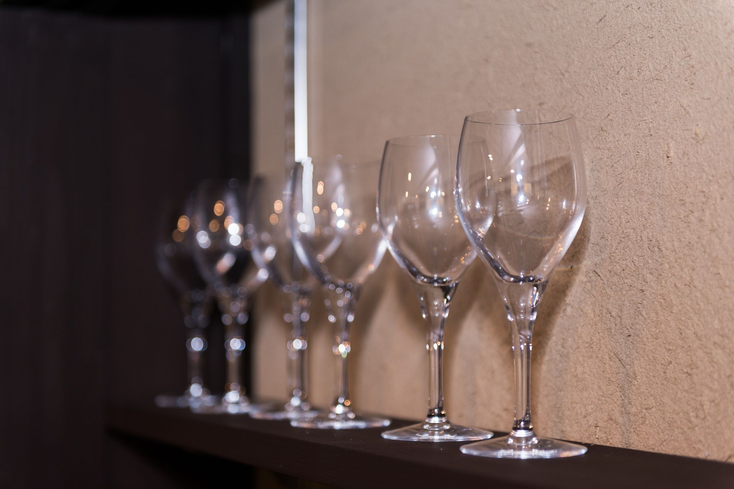 Une rangée de verres à vin vides, posés sur une étagère devant un mur à la texture particulière.