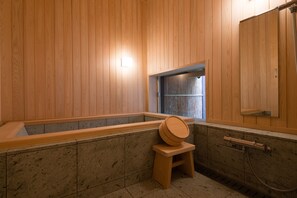 Una habitación con paneles de madera, una bañera, un taburete pequeño de madera, una ventana y un espejo.