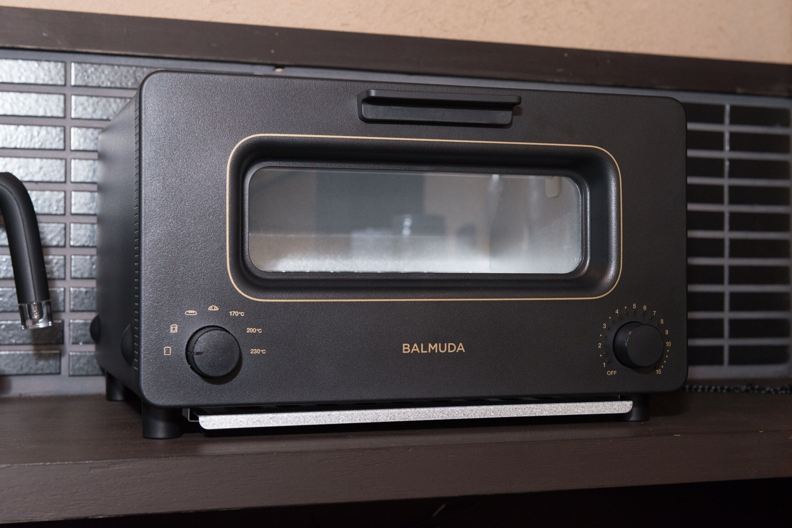 A black kitchen appliance with a digital display, a control knob, and a brand name 'BALMUDA'.