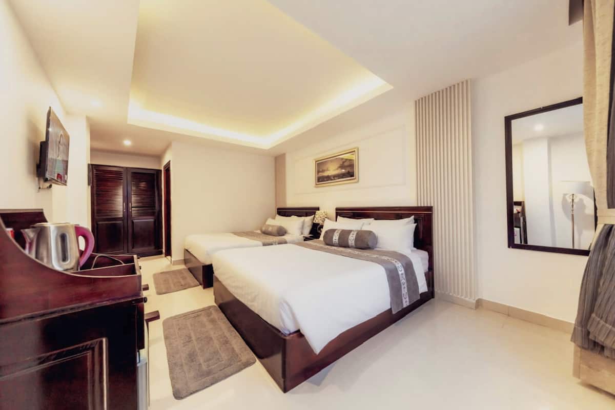 Une chambre d’hôtel avec deux lits, une commode en bois, un téléviseur à écran plat et un grand miroir.
