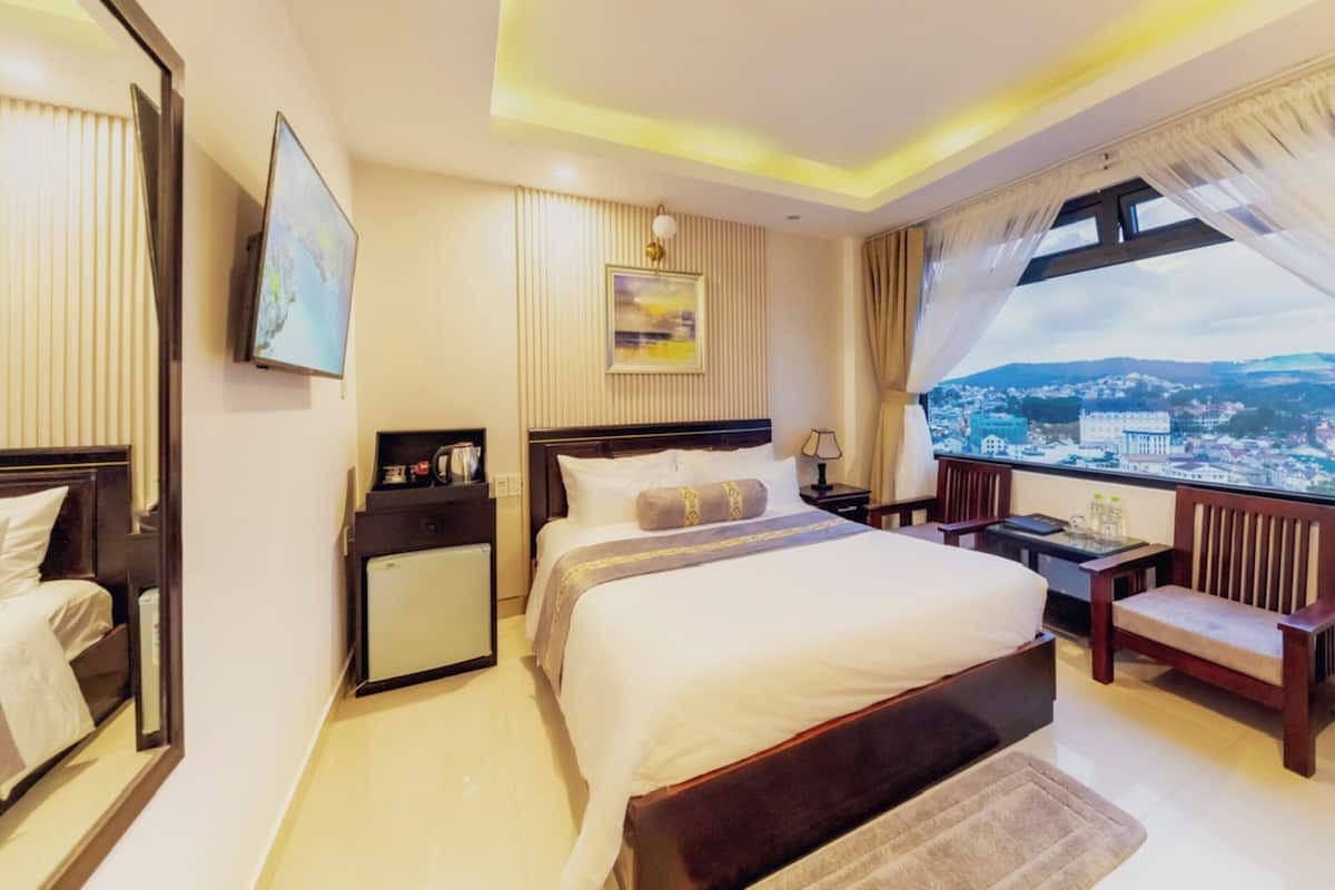 Une chambre d’hôtel avec un grand lit, un bureau, une chaise, une télévision, une petite table et une fenêtre donnant sur la ville.