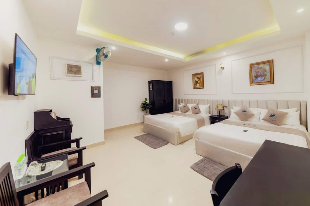 Une chambre d’hôtel avec deux lits, un bureau, une chaise, une télévision et un ventilateur de plafond.