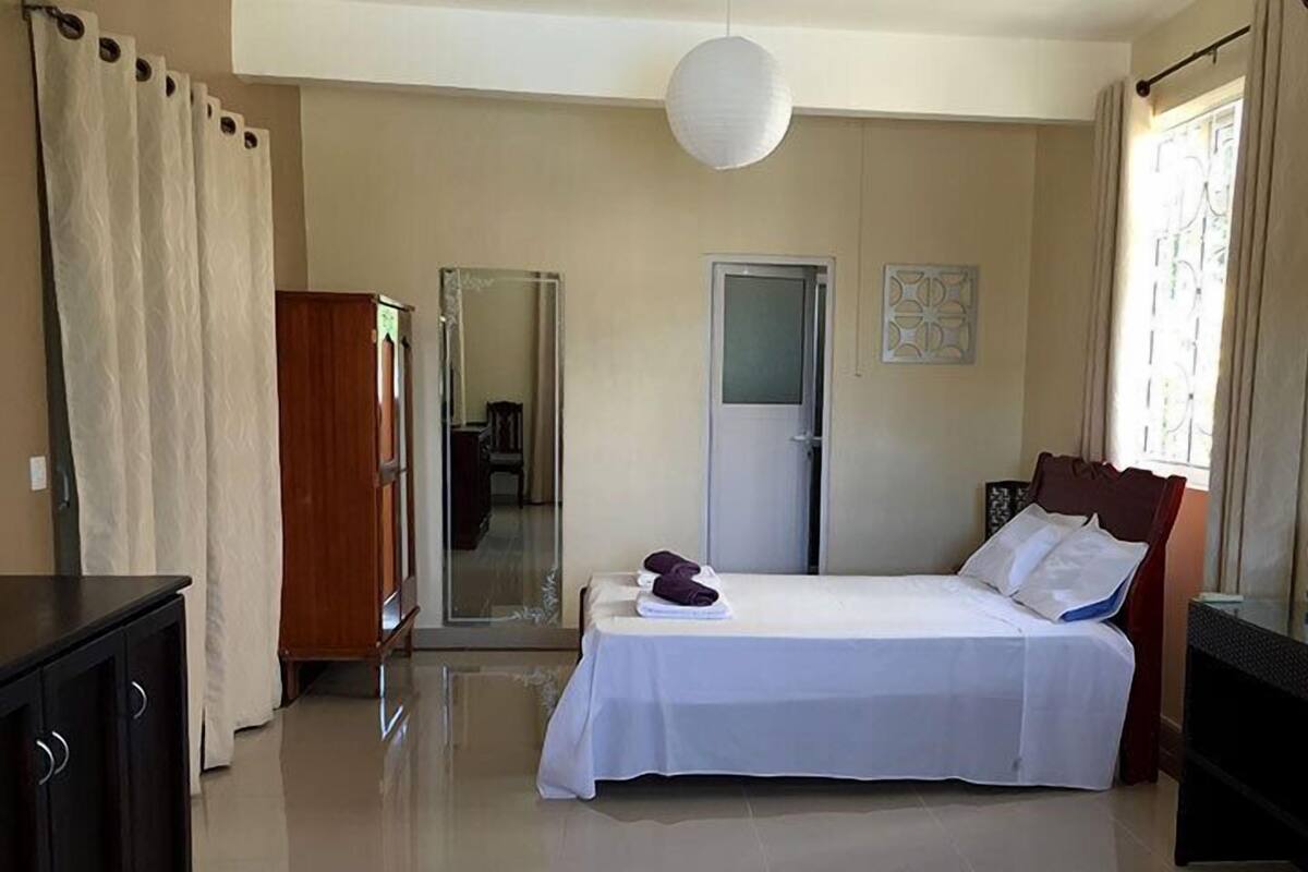 Una habitación de hotel con una cama, un armario, un espejo, una puerta y una ventana.
