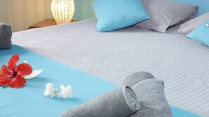 A neatly made bed with blue and grey bedding, a blue pillow, and a rolled grey towel on a blue bedspread. - Lariad BnB (Flic-en-Flac)