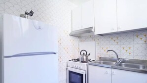 Eine kompakte Küche mit weißen Schränken, einem eingebauten Backofen, einem Herd und einem Spülbecken.