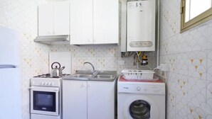 Eine kleine Küche mit weißen Schränken, einem Herd, einem Backofen, einer Spüle und einer Waschmaschine.