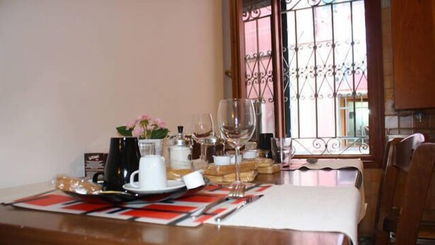 A dining table set with plates, glasses, and a coffee pot, with a window and decorative iron bars in the background. - Mario Apartment 1479 (Venice)