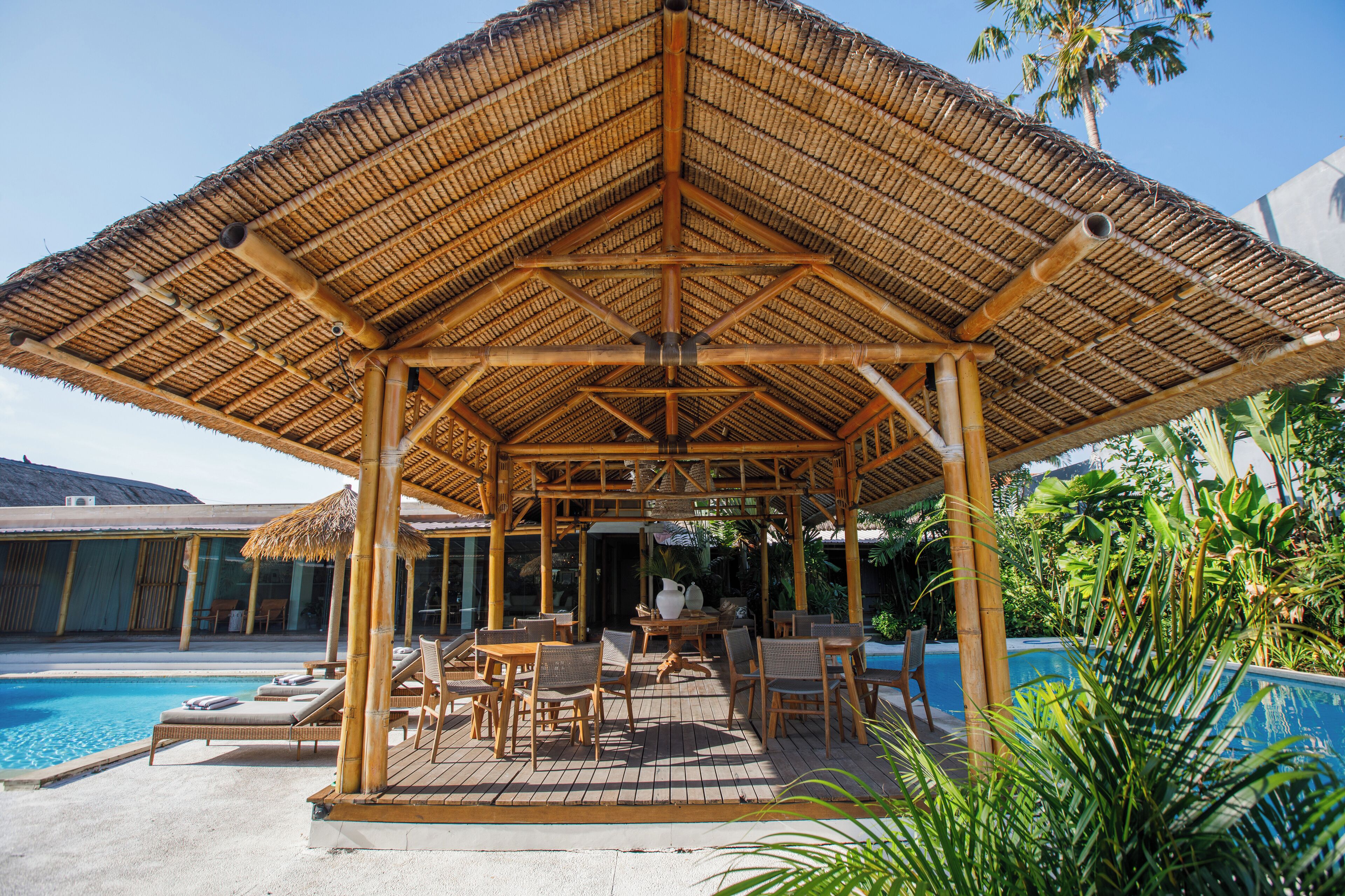 A covered outdoor seating area with bamboo furniture and a pool.