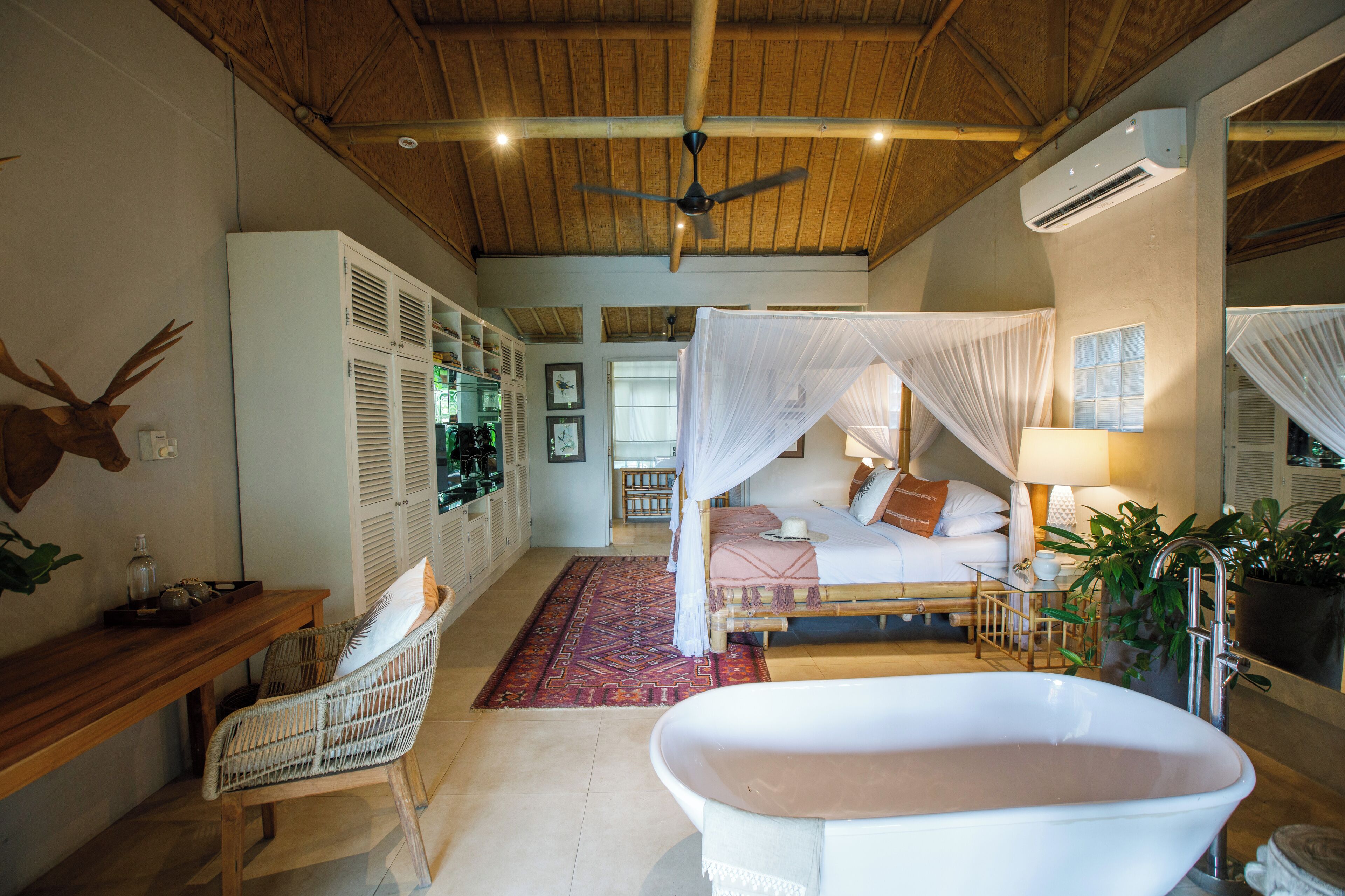 A spacious bedroom with a large bed, a sitting area with a chair, a bathtub, and a wardrobe.