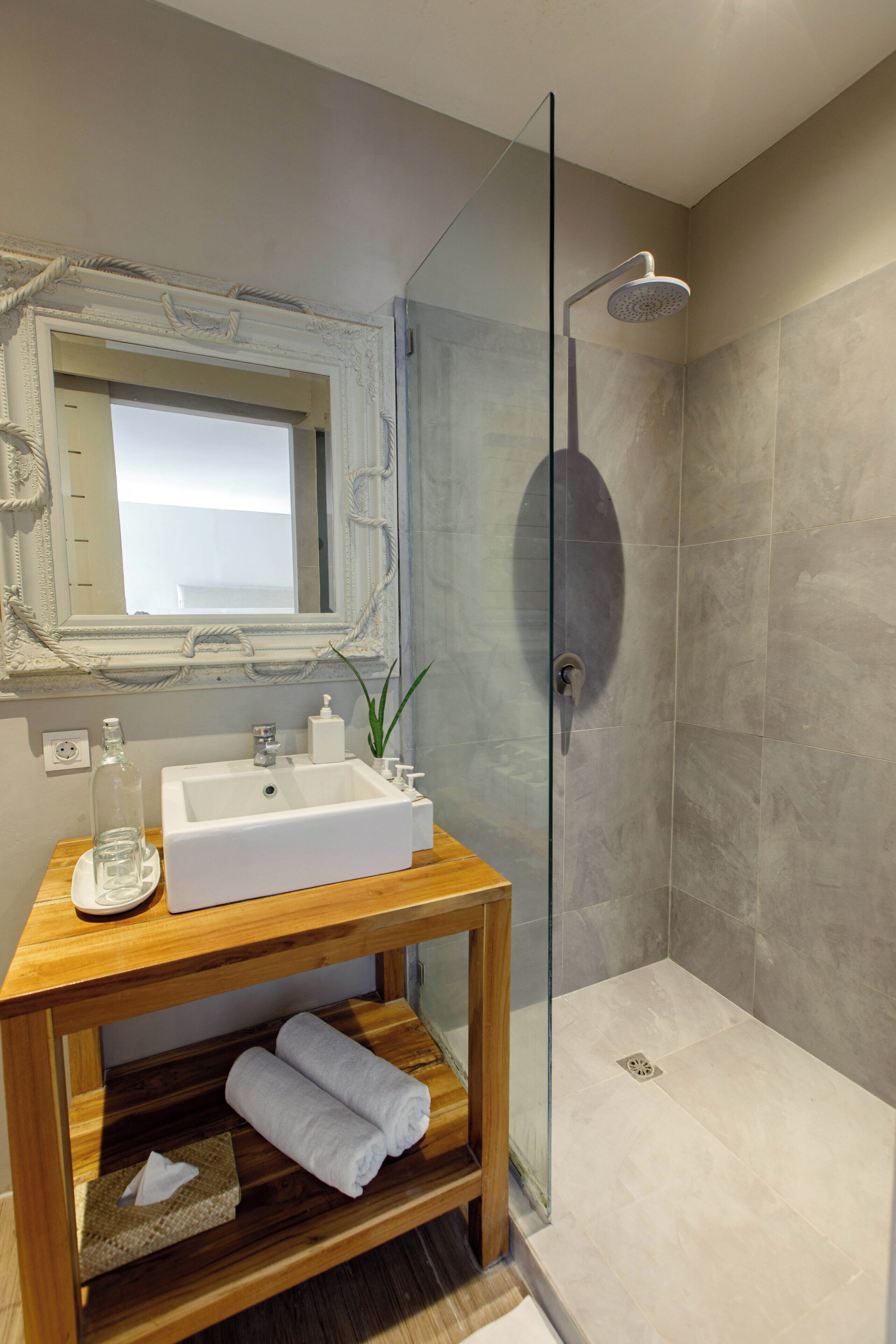 A modern bathroom with a glass-enclosed shower, a wooden vanity with a sink, and a mirror with an ornate frame.
