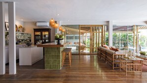 A spacious living area with a wooden floor, a central seating area with cushions, and a kitchen area with a green island and bar stools. - Bloomfield Umalas (Kerobokan)