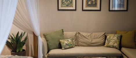 A living room with a sofa, a coffee table, and a potted plant. There are three framed pictures on the wall.