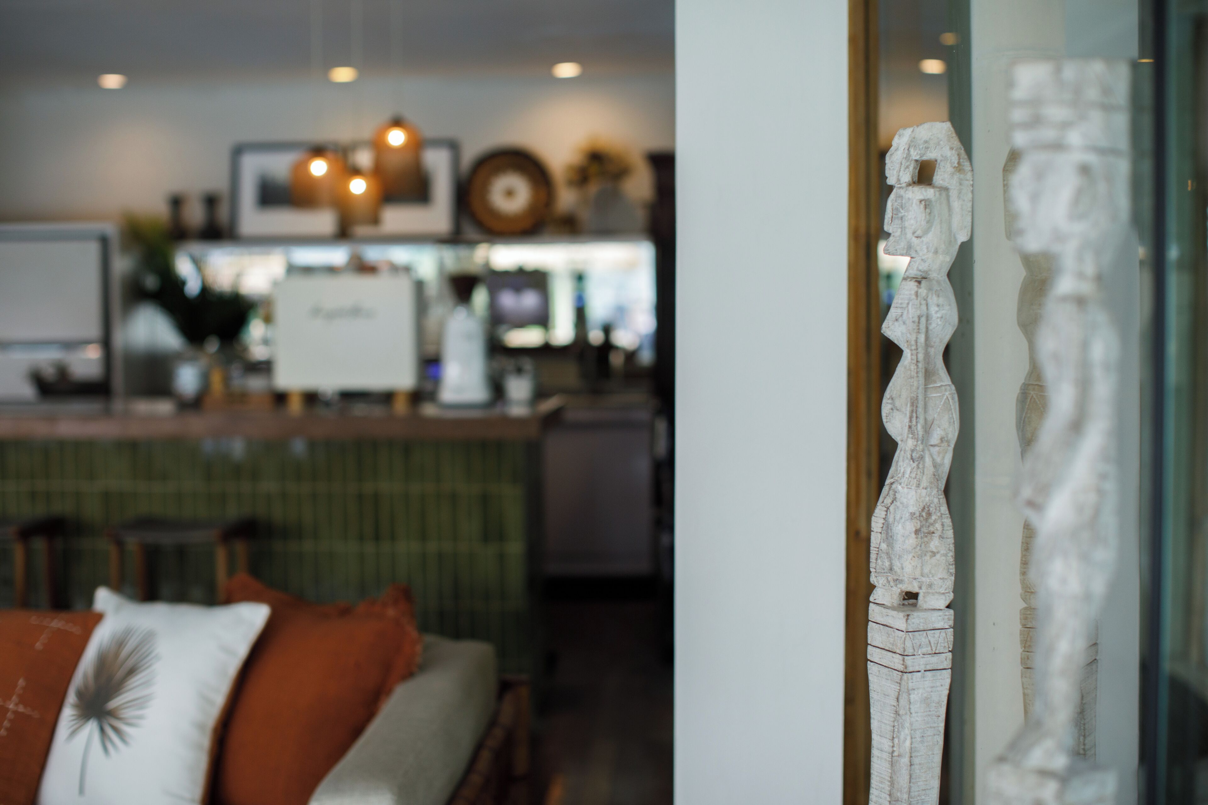 A modern interior with a bar area, a sofa with decorative pillows, and a sculpture on display.
