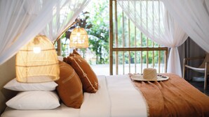 A bed with white and brown pillows, a straw hat, and a brown blanket. - Bloomfield Umalas (Kerobokan)
