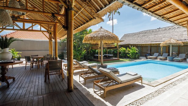 A poolside area with lounge chairs, a table, and a covered seating area with thatched umbrellas. - Bloomfield Umalas (Kerobokan)