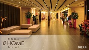 A hotel lobby with a modern design, featuring a central seating area, decorative plants, and a well-lit corridor.