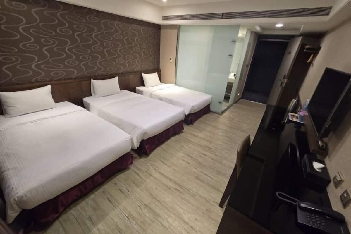 A hotel room with three beds, a desk, a phone, and a television.